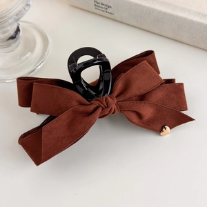 Close-up of brown suede bow hair claw clip with a delicate gold heart pendant detail