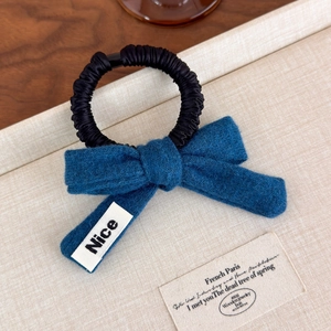 Detail of blue knitted bow hair scrunchie with Nice label on a beige textured tray