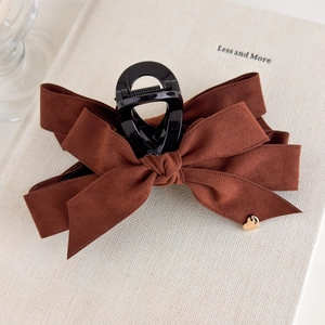 Detail of a large velvet bow hair claw in caramel brown with a gold heart charm