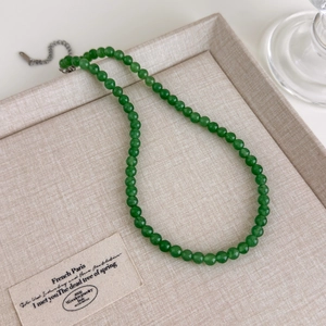Gros plan d'un collier de perles d'agate verte avec fermoir argenté sur plateau lin