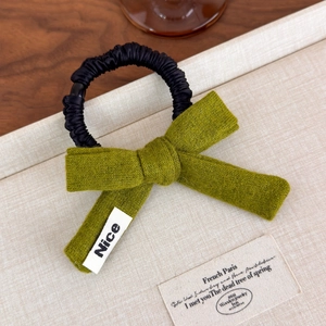 Close-up of grass green knit bow hair tie with a white Nice label and black elastic band