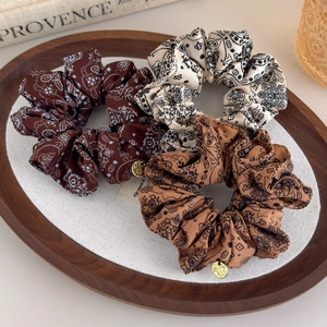 Three-piece paisley scrunchie set in brown and beige with gold charms on a tray