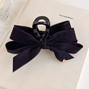 Detail shot of black velvet bow hair claw clip with golden heart ornament on book