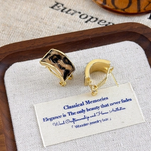 Detail of leopard print plush earrings with gold metal frame on a wooden jewelry tray