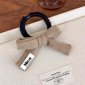 Detail of knitted bow hair tie with Nice label on light textured surface