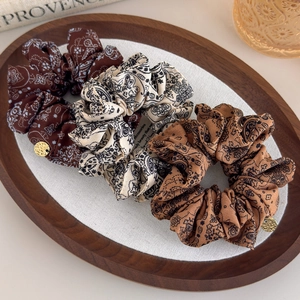 Detailed macro view of paisley print hair scrunchies with elegant gold metal charm accents