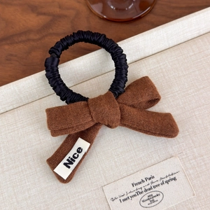 Detailed close-up of a brown knit bow hair scrunchie with a white Nice label tag