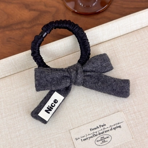Detailed macro view of dark grey wool bow scrunchie with white 'Nice' fabric label