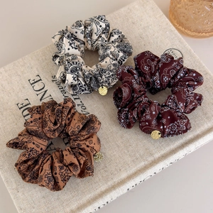 Three-piece paisley print scrunchie set with gold pendants on a rustic linen book background
