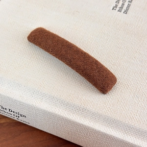 Detailed view of dark brown plush hair clip with soft wool texture on minimalist book