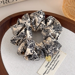 Detail of vintage paisley print scrunchie with a gold pendant on a wooden tray