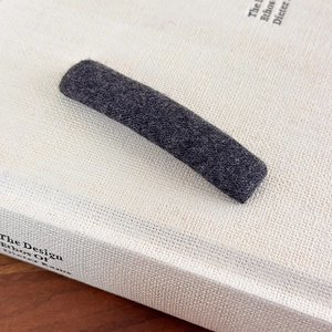 Detailed macro of a dark grey wool felt minimalist hair clip on a textured white book cover