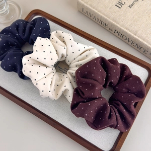 Three french style polka dot scrunchies in navy, cream and burgundy colors on a tray