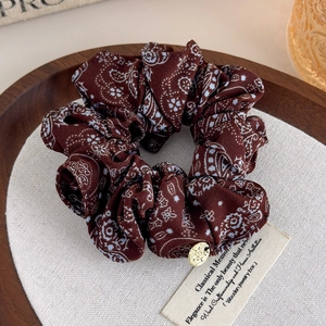 Close-up of retro paisley print scrunchie in dark red with a gold metal pendant