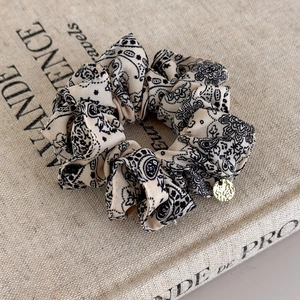 Macro view of paisley print scrunchie with a gold metal pendant on a vintage book