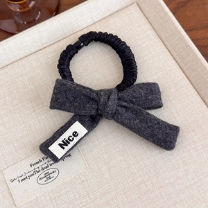 Detail of dark grey wool bow scrunchie with Nice label on a textured beige plate