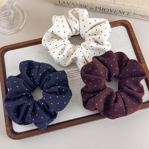 Close-up of three soft polka dot scrunchies in cream navy and brown on a wooden tray