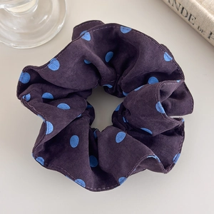 Detailed close-up of dark purple scrunchie with light blue polka dots on soft fabric