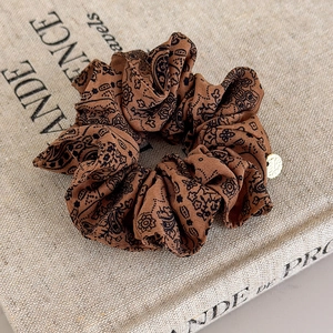 Close-up of brown paisley fabric scrunchie with a gold metal charm on a book