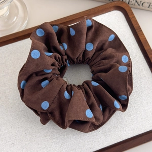 Detailed view of dark brown scrunchie with light blue polka dots and matte texture finish