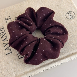 Detailed texture of burgundy polka dot fabric scrunchie on a beige linen book