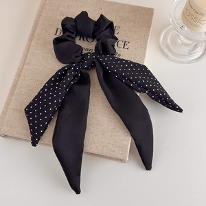 Close-up of elegant black satin polka dot bow hair tie on a minimalist book background
