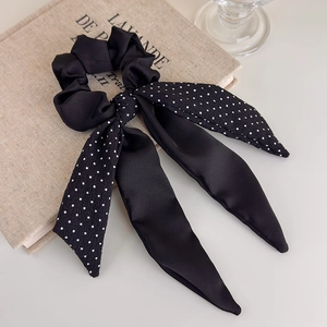 Detail of a black satin scrunchie with polka dot bow on a soft fabric book background