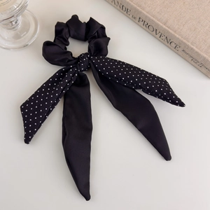 Detail of elegant black satin hair scrunchie with polka dot ribbon on beige background