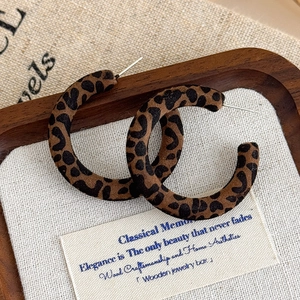 Dettaglio di orecchini a forma di C con stampa leopardata su vassoio di legno