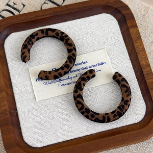 Dettaglio di orecchini a cerchio a C con stampa leopardata su vassoio in legno