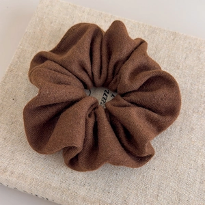Détail d'un chouchou en tricot marron foncé sur un tissu beige à la texture douce et moelleuse