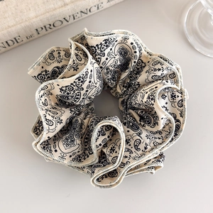Detailed view of paisley pattern on beige fabric scrunchie with elegant wavy edges