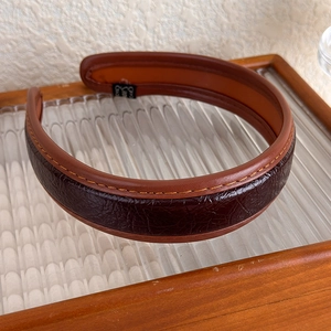 Détail d'un serre-tête large en cuir PU avec texture craquelée marron et surpiqûres jaunes