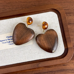 Macro shot of vintage wooden heart earrings with amber resin studs on a wooden tray