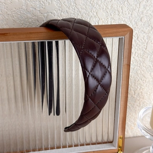 Détail d'un serre-tête large en similicuir marron matelassé sur cadre bois