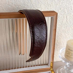Gros plan du bandeau en cuir marron foncé avec plis texturés et coutures orange contrastées