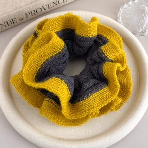 Detail of yellow and black knit scrunchie with subtle golden thread on a beige tray