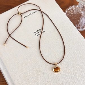 Detail of tiger eye pendant on adjustable brown leather cord against a white book