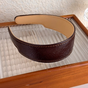 Détail d'un serre-tête en cuir PU marron avec texture à carreaux et coutures jaunes