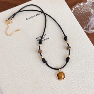 Detail view of tiger eye stone pendant on black braided cord with golden metal beads