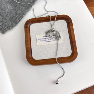 Detail of silver horse pendant with tassels on snake chain over a cozy wooden tray