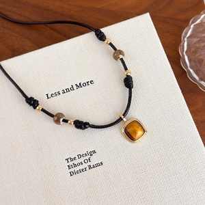 Macro shot of tiger eye stone pendant on black cord necklace with golden beads