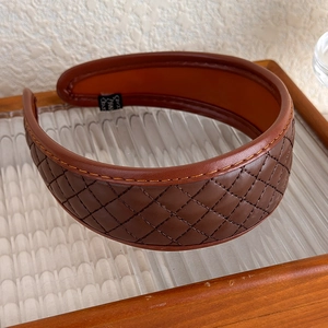 Détail macro du serre-tête en cuir PU marron avec surpiqûres losanges sur plateau