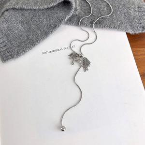 Detail of silver horse pendant with tassel design on snake chain over grey knit sweater