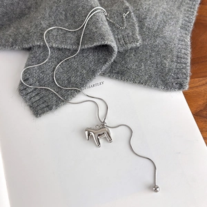 Detail of silver horse pendant on snake chain over grey knit sweater background