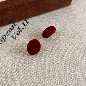 Dettaglio di orecchini a sfera in velluto rosso con perni dorati su lino beige naturale
