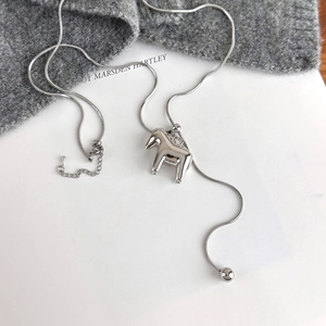 Macro detail of silver Dala horse pendant on snake chain over a white and grey background