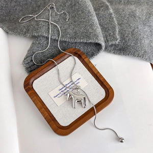Detail of silver Dala horse pendant on a sleek snake chain over a cozy grey knit background