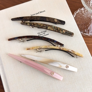 Minimalist acetate hair clip set with gold emblem on white textured book backdrop