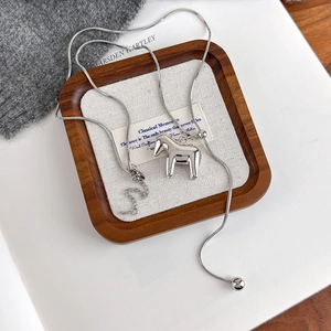 Close-up of silver Dala horse pendant on snake chain over walnut wooden tray